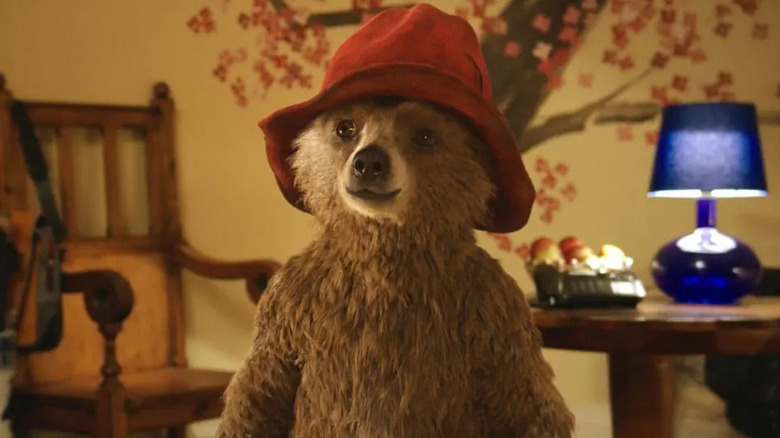 Paddington sans chemise debout dans la maison Brown portant son chapeau rouge à Paddington