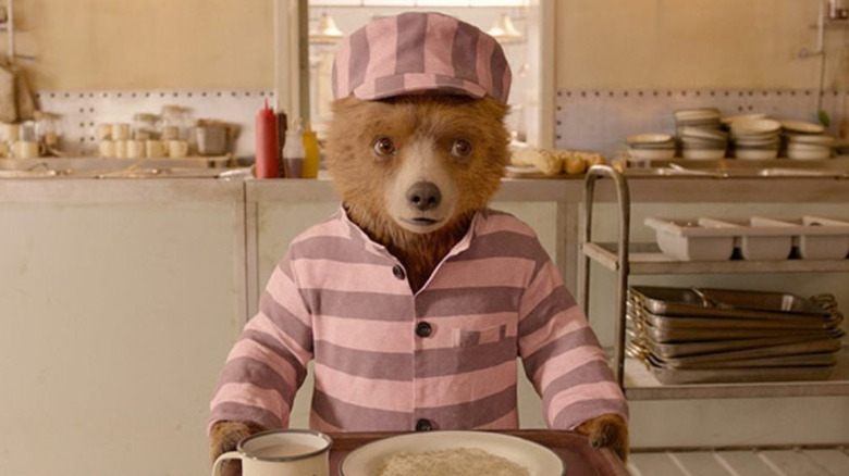 Paddington dans son uniforme de prison tenant un plateau et ayant l'air confus dans Paddington 2