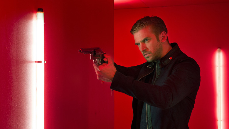 David pointant un revolver sous les feux rouges dans The Guest (2014)