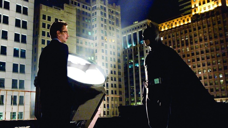 Le commissaire Gordon et Batman debout à côté du Bat-Signal dans Batman Begins (2005)