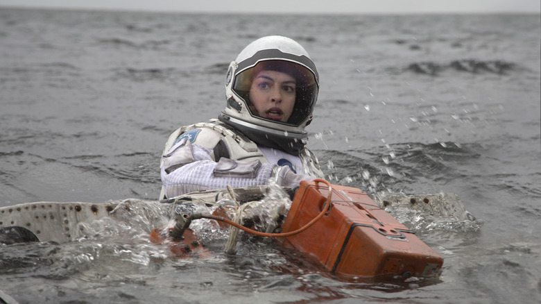 Dr. Amelia Brand se débat dans l'eau dans une combinaison spatiale, tenant une boîte orange, dans Interstellar (2014)
