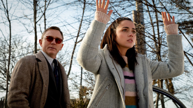 Marta Cabrera levant les mains tandis que Benoit Blanc se tient derrière elle avec des lunettes de soleil dans Knives Out (2019)