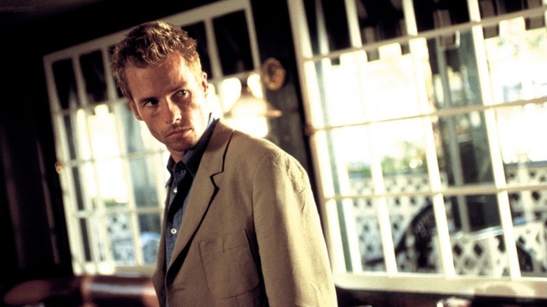 Leonard debout de travers dans un bar, vêtu d'un costume beige et d'une chemise bleue, dans Memento (2000)